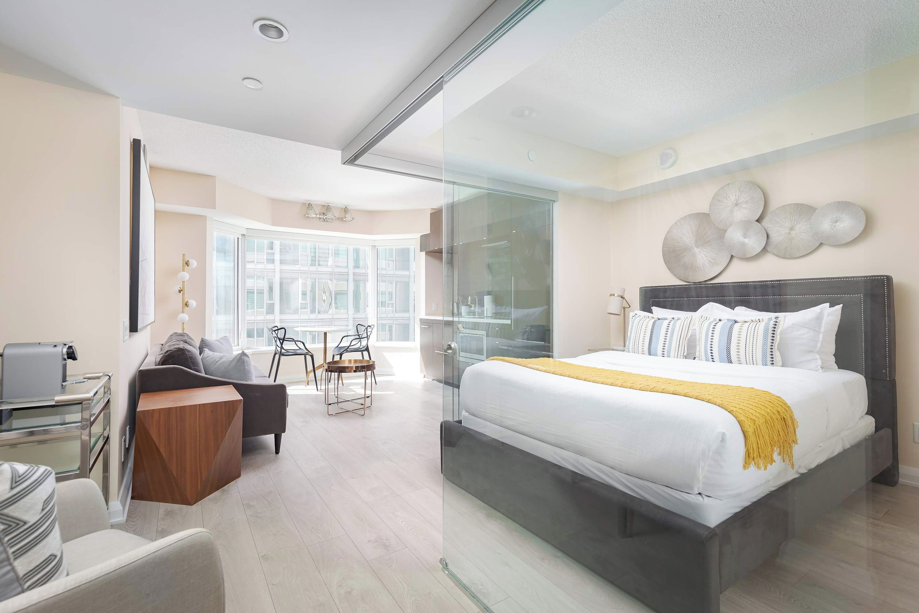 A modern hotel room with a large bed, a desk, a chair, and a glass partition.