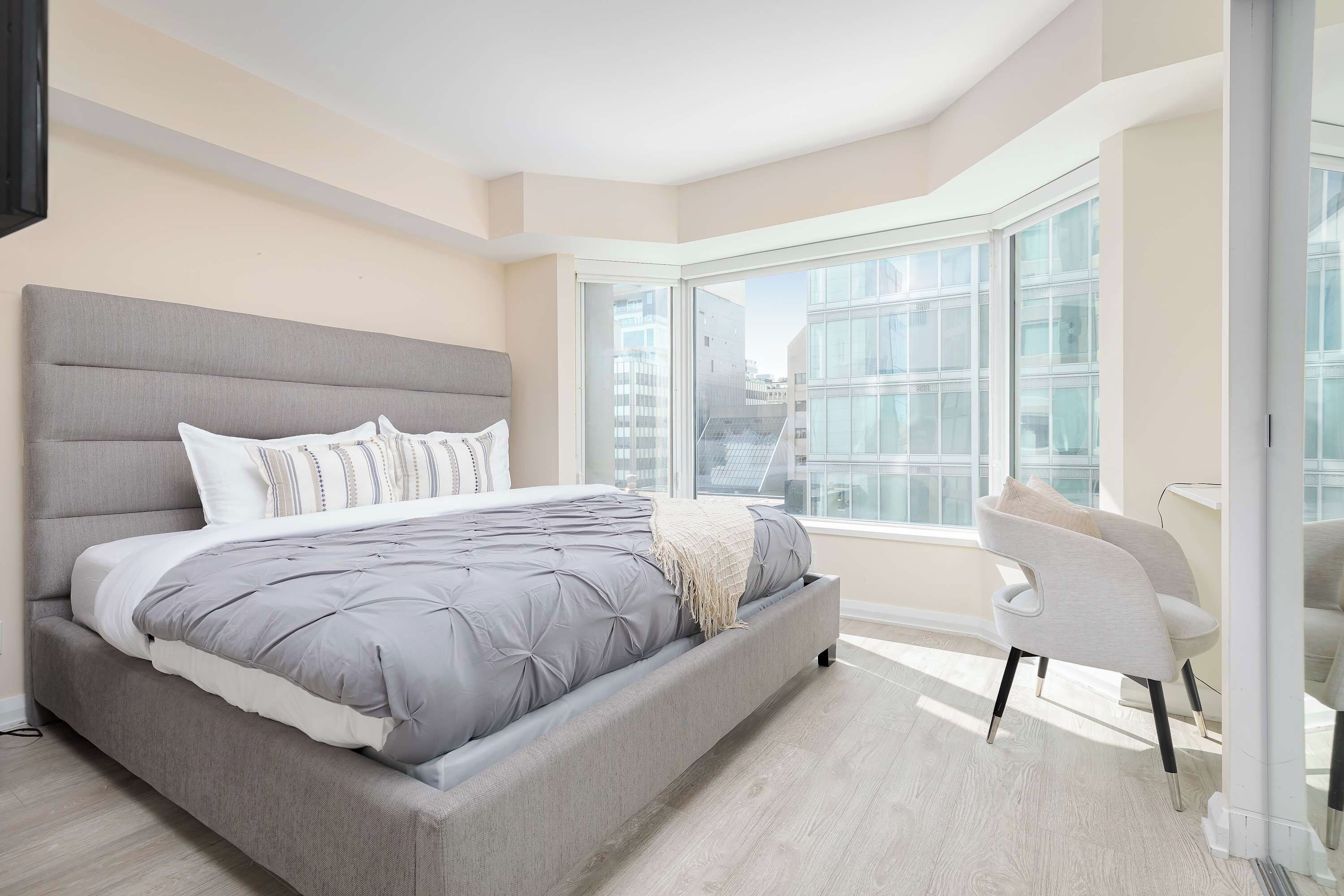 A modern bedroom with a large bed, a seating area, and a view of the city through large windows.