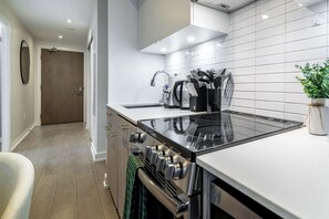 Eine moderne Küche mit einem schwarzen Induktionskochfeld, Edelstahlgeräten und einer weißen Fliesenküchenwand.