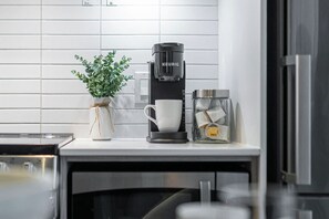 Keittiössä on kahvinkeitin, kuppi ja teepurkki työtasolla.