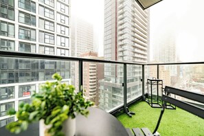 A balcony with a view of high-rise buildings, a small exercise area with a bench, and a potted plant. - Downtown 3BR, Balcony & City Views (Toronto)
