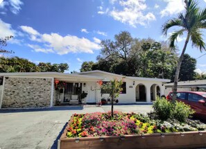 A two-story building with a stone facade, a covered porch, and a small garden with colorful flowers. - Private King Suite 4-Min Walk to Wilton Drive (Wilton Manors)