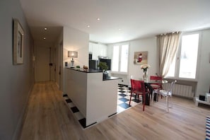 A modern kitchen with a central island, a dining area with a checkered floor, and a view of the city through large windows. - New Listing (Bordeaux)