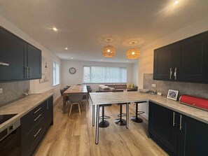 A modern kitchen with dark cabinetry, a central island with stools, and pendant lighting. - Newly refurbished modern house with parking, ideally situated & sleeps up to 8! (Mevagissey)