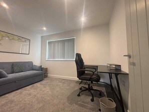 A room with a grey sofa, a black office chair, a desk, a map on the wall, and a window with blinds. - Newly refurbished modern house with parking, ideally situated & sleeps up to 8! (Mevagissey)