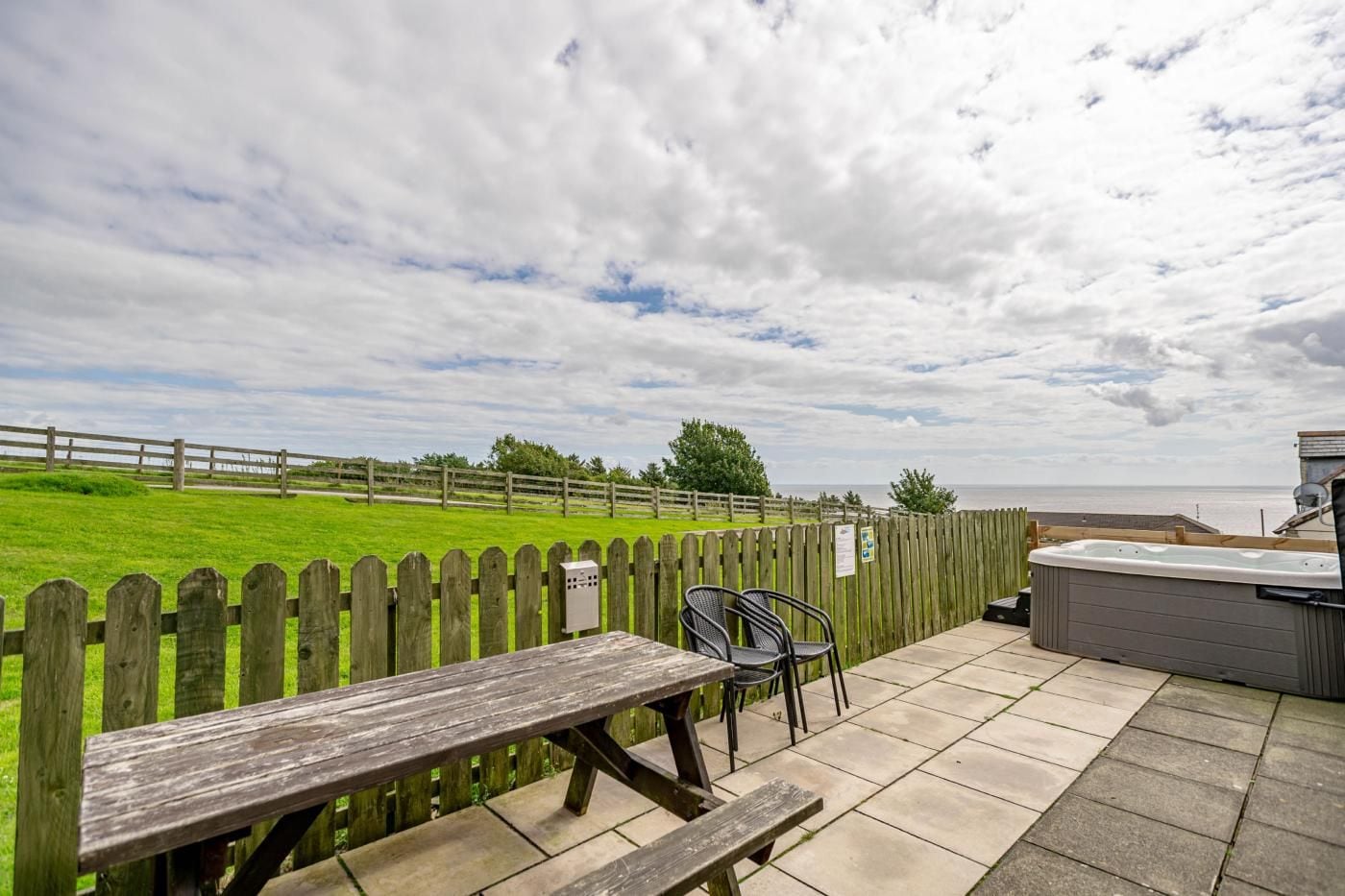 An outdoor patio with a wooden fence, a hot tub, and a picnic table.
