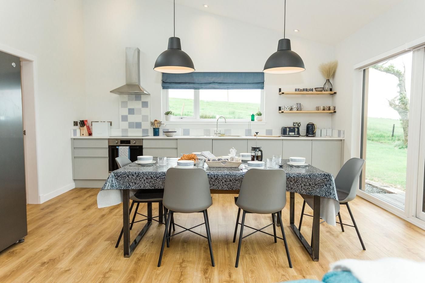 Une cuisine moderne avec une table à manger pour quatre personnes, dotée d’un plan de travail en granit, de chaises noires et d’un éclairage suspendu.