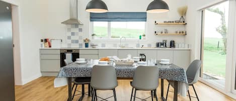 Een moderne keuken met een eettafel voor vier personen, met een granieten aanrechtblad, zwarte stoelen en hanglampen.