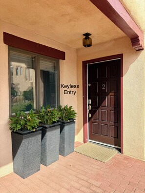 A building entrance with a door marked 'Keyless Entry' and three planters with green plants. - Walk to Plaza, 2BR/2.5BA Townhouse, Best for extended vacation, relocation, LANL (Santa Fe)
