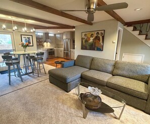 A modern living room with a sectional sofa, a dining area with bar stools, a kitchen with stainless steel appliances, and a staircase leading to an upper level. - Walk to Plaza, 2BR/2.5BA Townhouse, Best for extended vacation, relocation, LANL (Santa Fe)