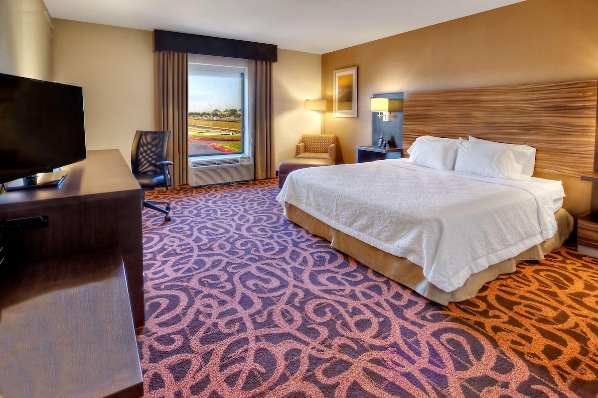 Quarto de hotel com cama, escrivaninha, cadeira, televisão e janela com vista.
