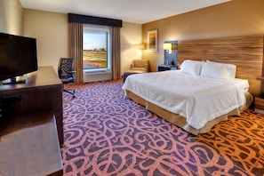 Quarto de hotel com cama, escrivaninha, cadeira, televisão e janela com vista.