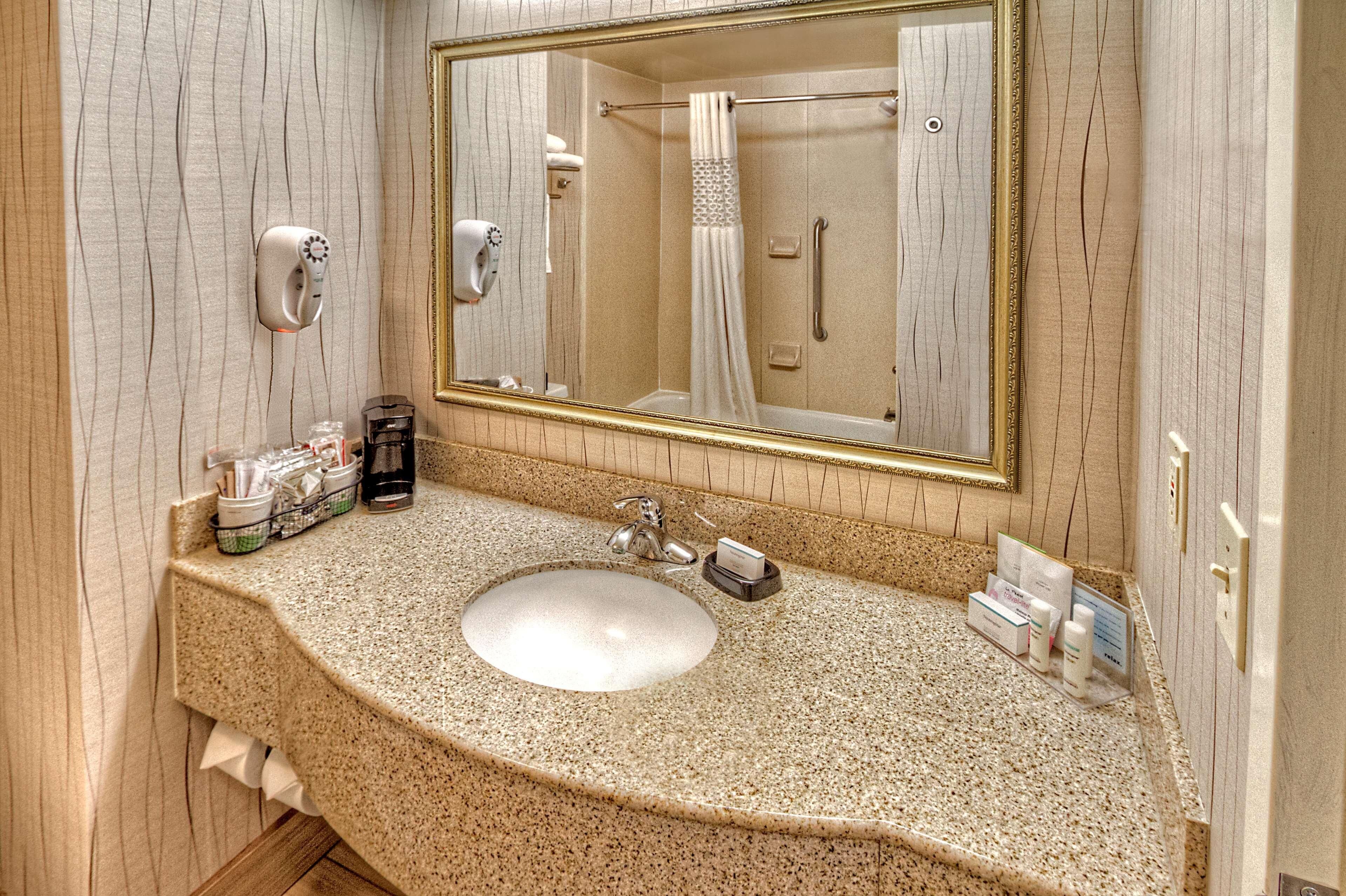 A bathroom with a granite countertop, a sink, a mirror, and a shower.