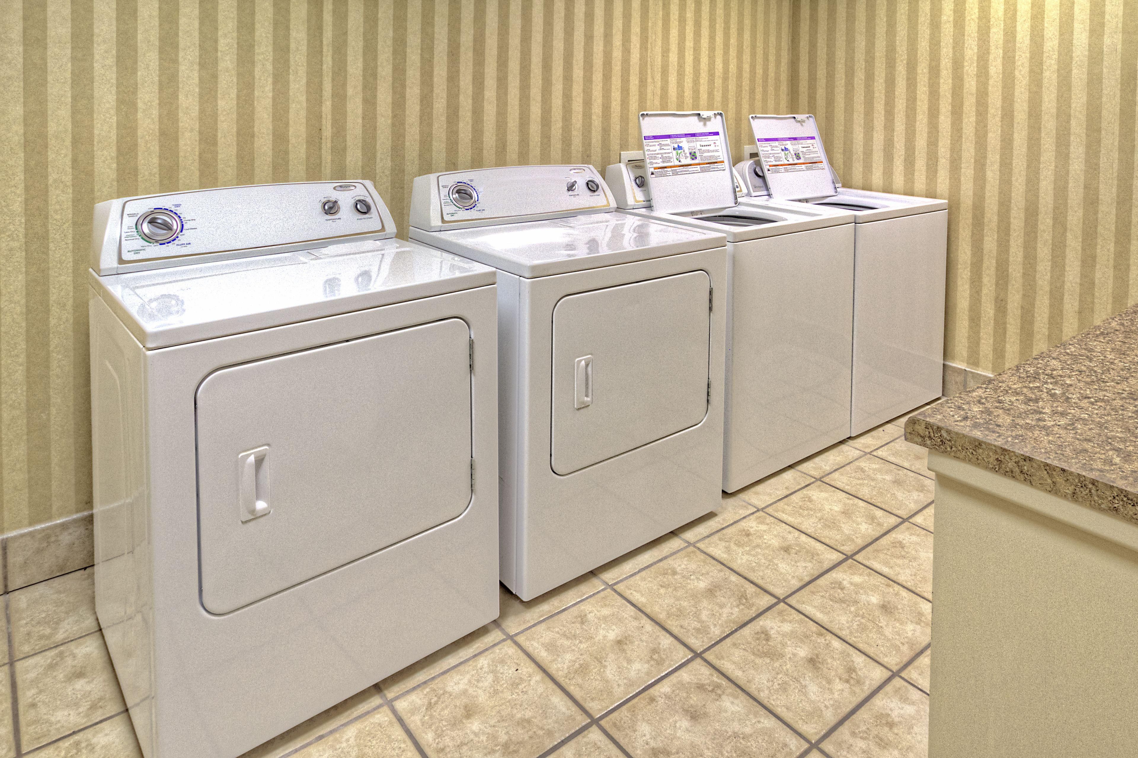 A row of white front-loading washers and dryers in a laundry room with striped wallpaper and tiled flooring.