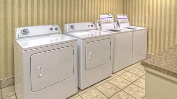 A row of white front-loading washers and dryers in a laundry room with striped wallpaper and tiled flooring.