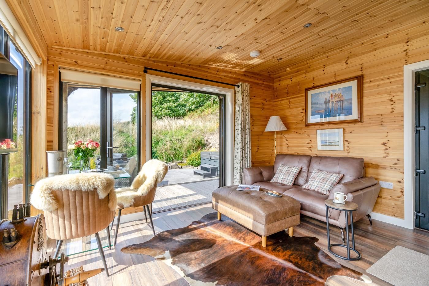 A cozy room with a leather sofa, a fur-covered chair, and a glass table with flowers.