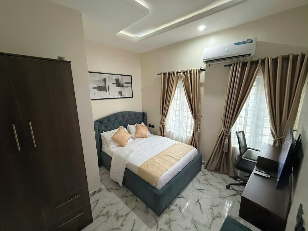 A hotel room with a bed, a desk, an air conditioner, and curtains.