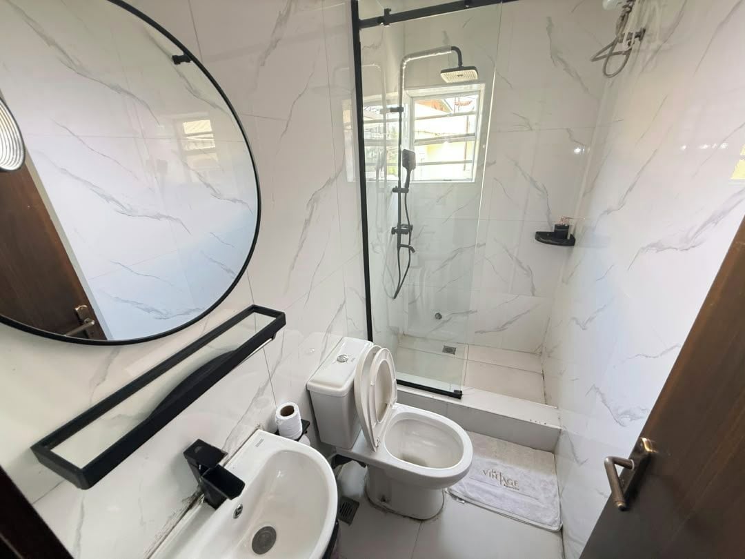 A bathroom with a toilet, sink, mirror, shower, and a glass-enclosed shower area.