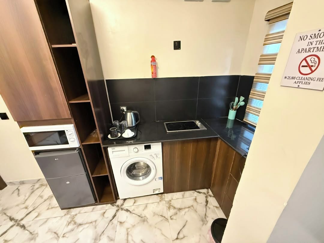 A compact kitchen with a washing machine, microwave, and a small refrigerator.