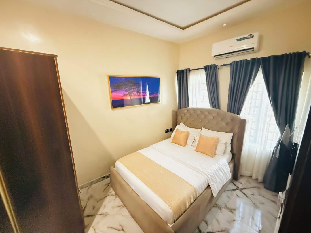 A bedroom with a bed, a painting, an air conditioning unit, and curtains.