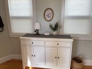A white dresser with two drawers and two doors, a lamp, a framed picture, and a plant on top. - Boston Urban Nests U4: Long Term 1 Month + (Boston)