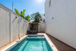 A swimming pool with a tiled deck, a barbecue area, and a white wall with a window. - House in Condo. w/ Pool & BBQ Fae0003 (Porto Seguro)