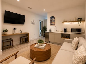 A modern living room with a flat-screen TV, a round coffee table with a book, a sofa, and a kitchen area with a microwave and coffee maker. - Enjoyable 1-bedroom apartment in peaceful Miami neighborhood (Miami)