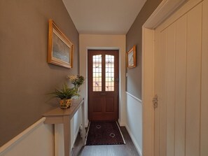 A hallway with a wooden door, a white console table with a vase of flowers, and a patterned rug leading to a room. - 2 Bed in Hordle (oc-m46569) (Hordle)