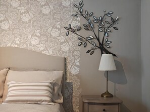 A bedroom with a floral wallpaper, a bed with striped pillows, a nightstand with a lamp, and a decorative metal tree. - 2 Bed in Hordle (oc-m46569) (Hordle)