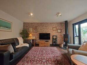A living room with a brick wall, a fireplace, a flat-screen TV, a sofa, and a patterned rug. - 2 Bed in Hordle (oc-m46569) (Hordle)