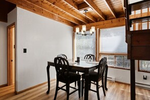 A dining area with a wooden table and chairs, a chandelier, and large windows with blinds. - Premium Cabana - Outdoor Jacuzzi (Tijeras)