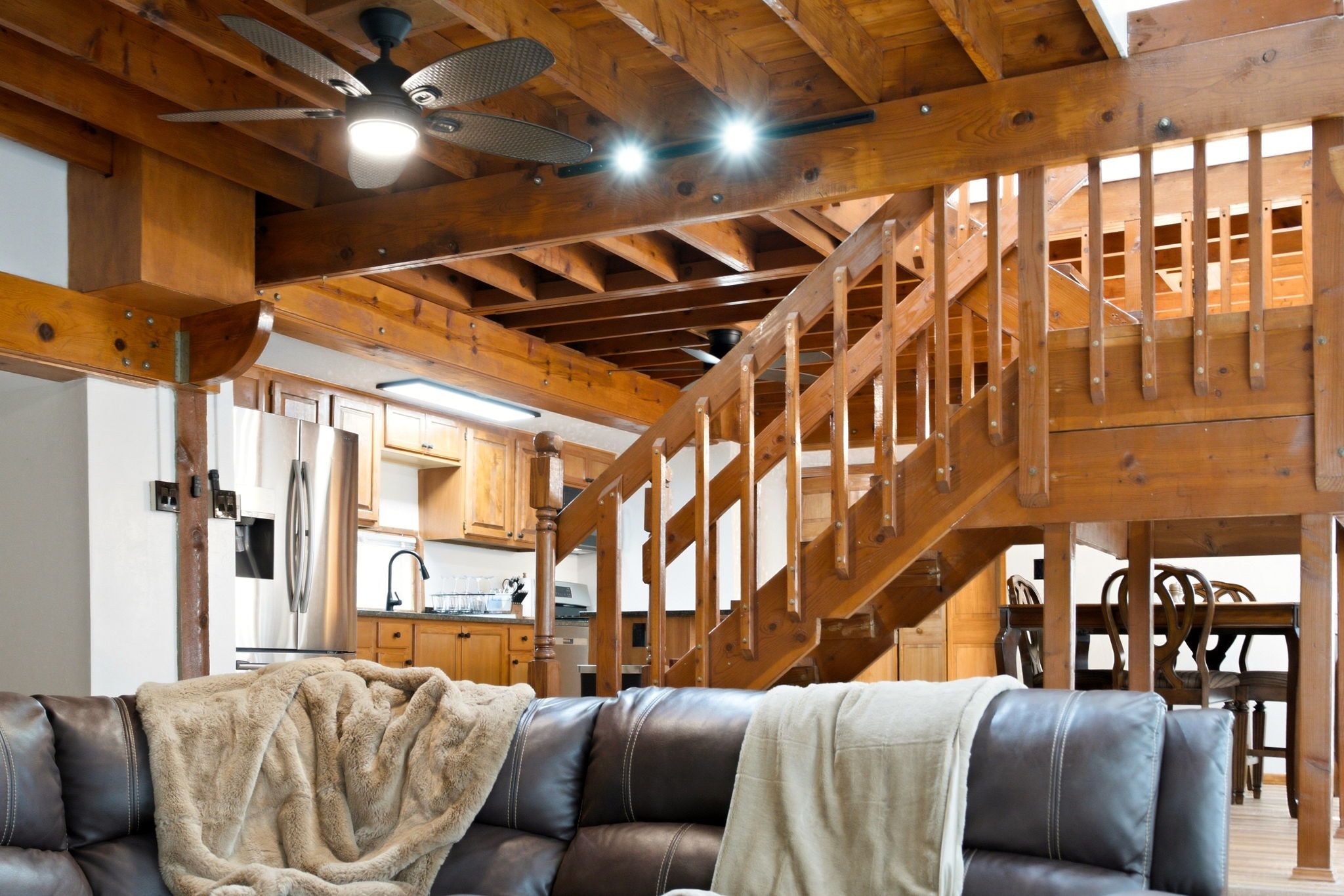 Un interior de madera con una escalera, un sofá de cuero y una zona de cocina.