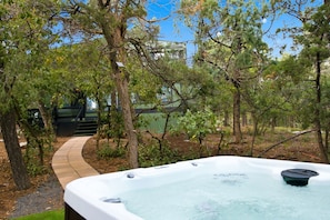 A hot tub surrounded by trees and a pathway leading to a building.
