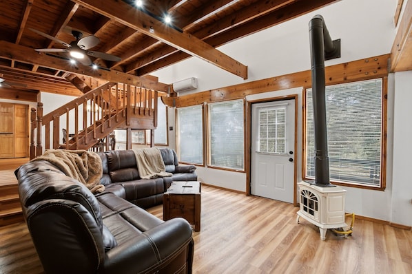 A cozy living room with a leather sofa, a wooden staircase, and a wood-burning stove.