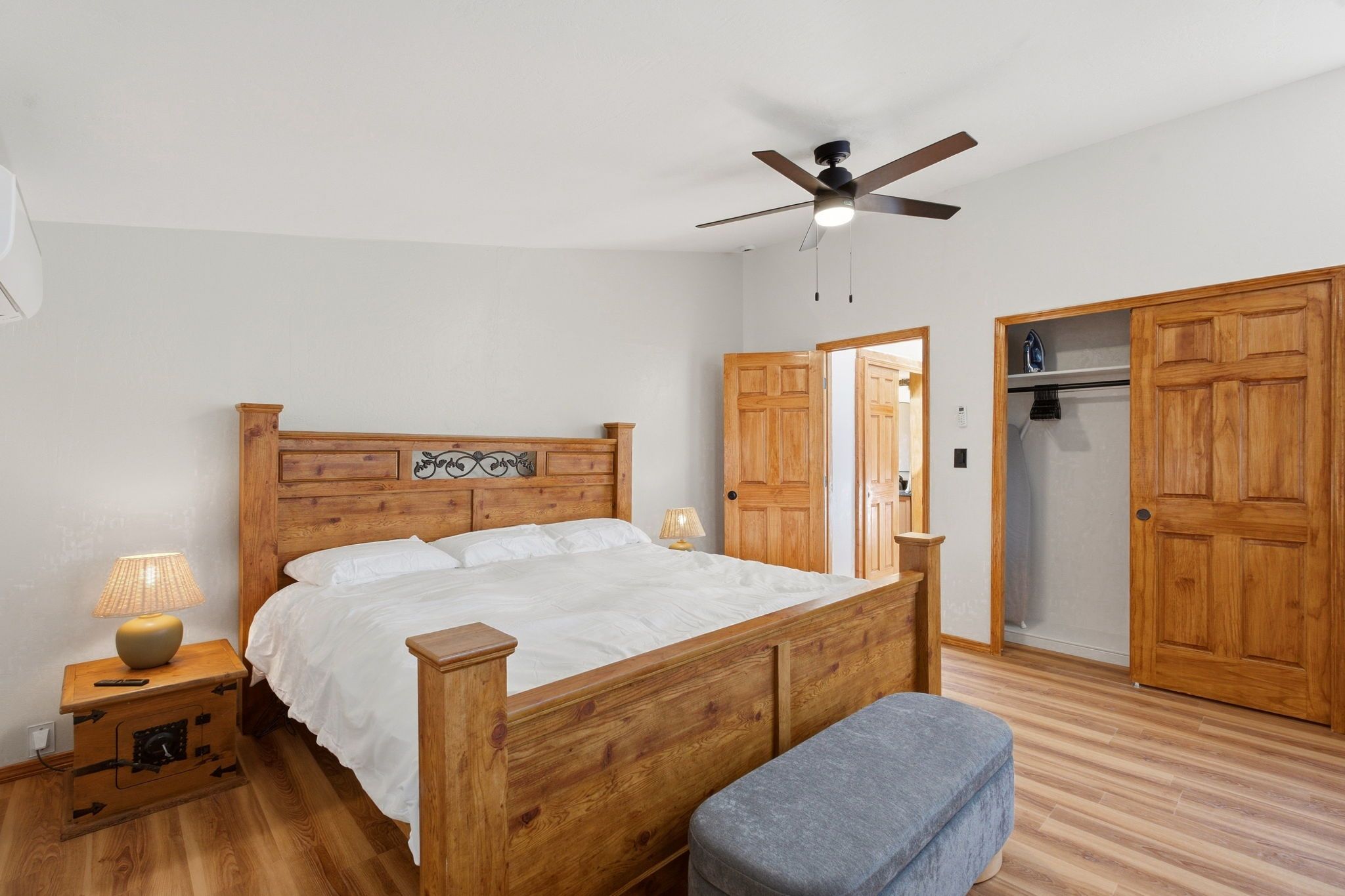 Un dormitorio con cama de madera, ventilador de techo, armario y una banca.