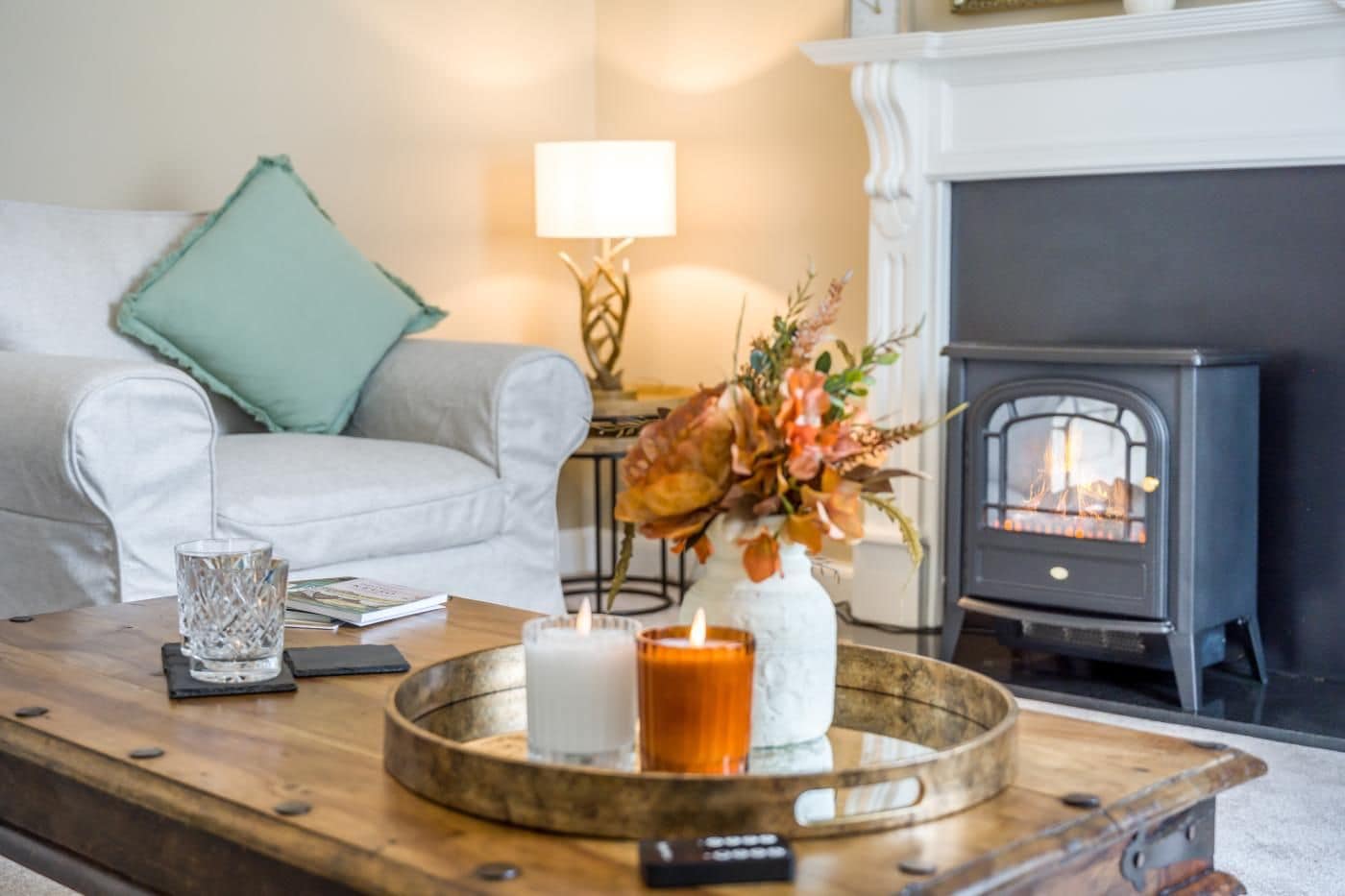 Ein gemütliches Wohnzimmer mit Kamin, einer Couch, einem Couchtisch mit Kerzen und einem Blumenstrauß.