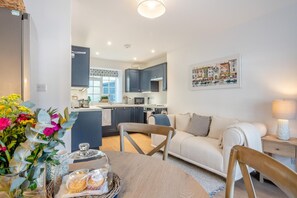 A modern kitchen with dark cabinets, a dining area with a table set for two, and a living room with a sofa and a lamp. - 2 Bed in Kelso (oc-k46033) (Kelso)