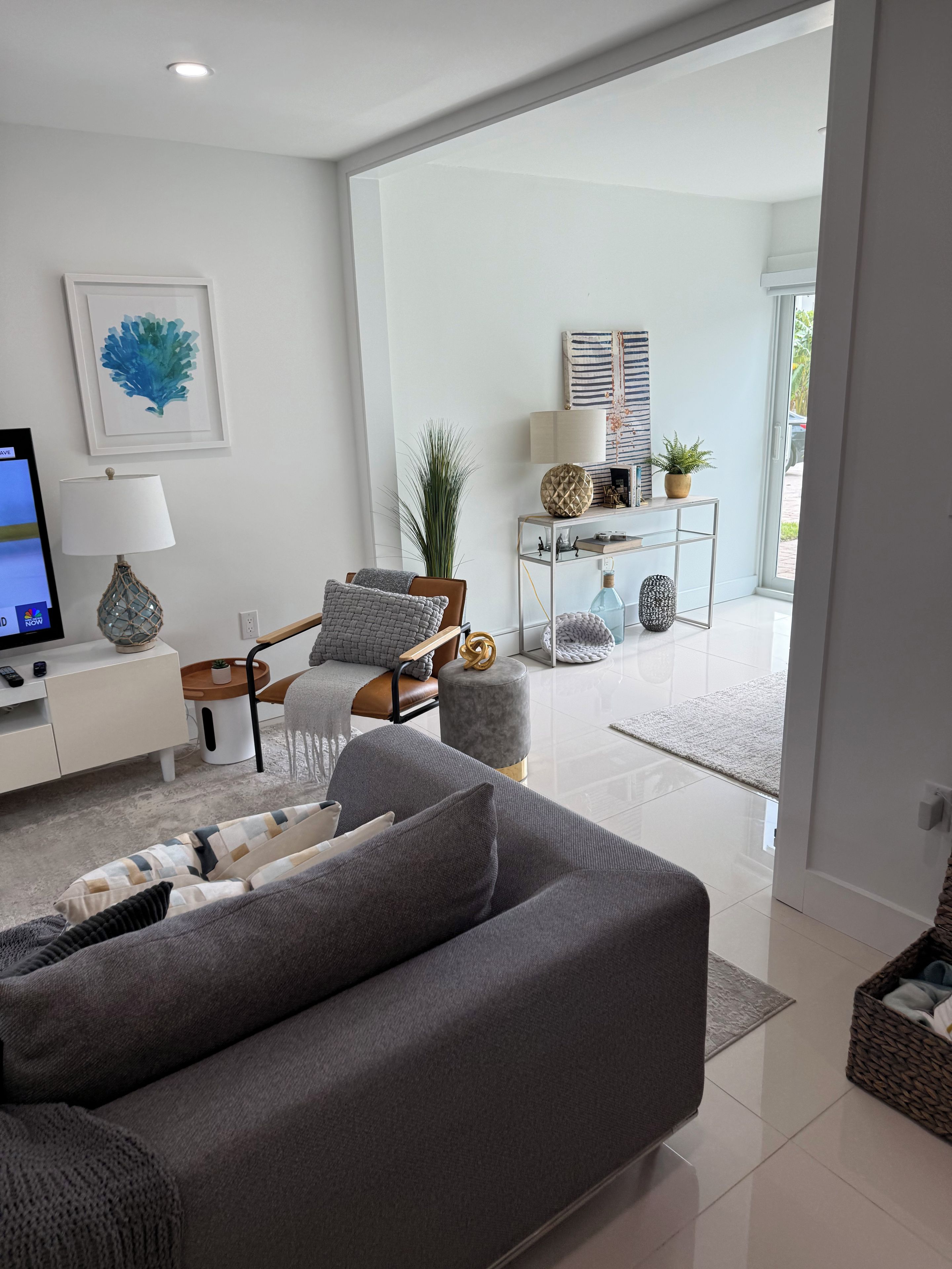 Un salon moderne avec un canapé gris, une chaise en bois, une table d’appoint avec une lampe et un téléviseur.