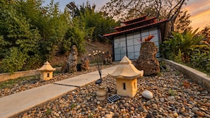 A garden with stone lanterns, a pathway, and a building with a red roof.