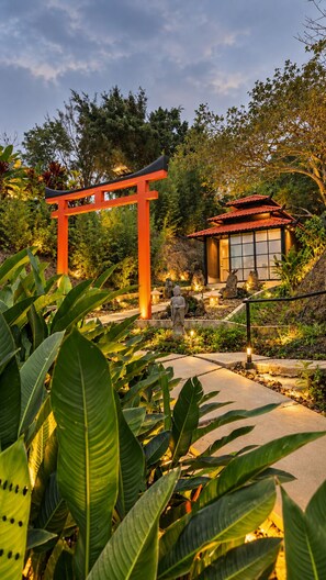 A traditional Japanese torii gate leading to a building with a tiled roof, surrounded by lush greenery and stone pathways.