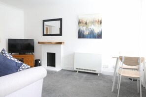 A modern living room with a flat-screen TV, a fireplace, a radiator, and a painting on the wall. - 1 Bed in Crieff (oc-d634970) (Crieff)
