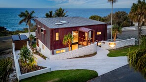 A modern house with a stone pathway leading to the entrance, a view of the ocean, and a well-maintained garden. - The Kopper House: Luxury in 1770 (1770)