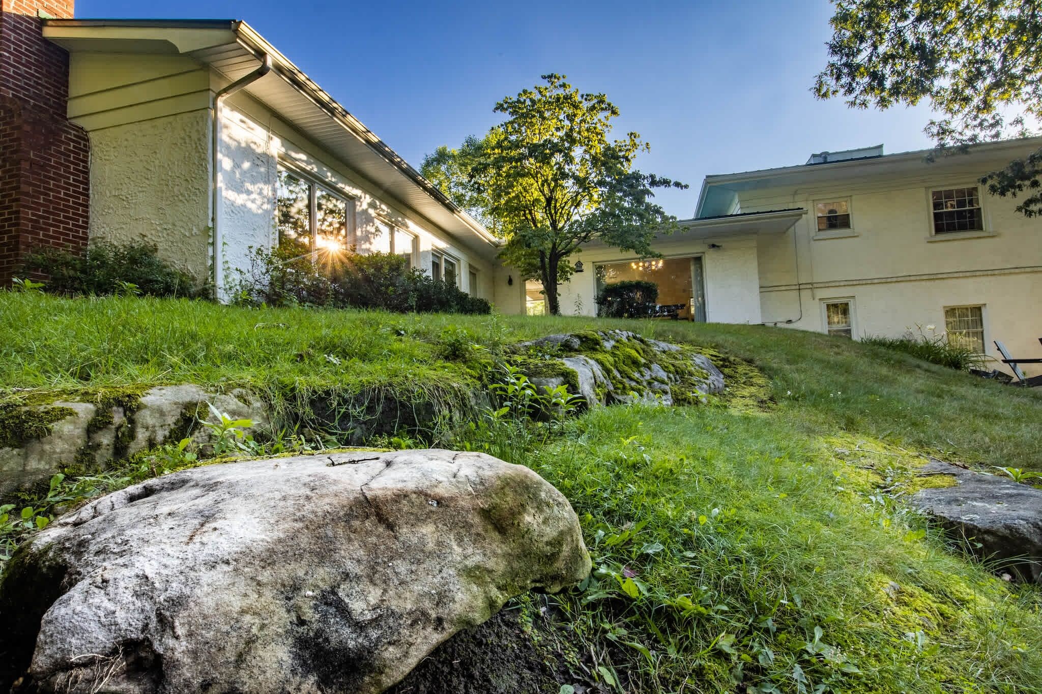 A building with a sloped roof, a grassy yard, and a large rock in the foreground.