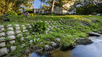Een met stenen beklede beek met gras en planten, een gebouw op de achtergrond en een heldere lucht.