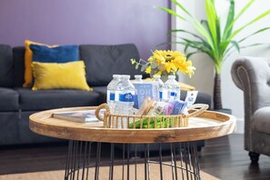 Ein runder Couchtisch aus Holz mit einem gewebten Korb, der Wasserflaschen, eine Zeitschrift und eine Vase mit gelben Blumen enthält.