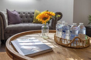 A round wooden table with a magazine, a vase with sunflowers, and water bottles. - Stylish 2BR | Near City Centre | FREE Parking (Reading)