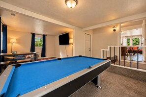 Een pooltafel in een kamer met een televisie, een bank en een eethoek.