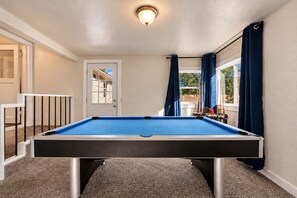 Una mesa de billar con superficie de fieltro azul, una puerta con ventana y cortinas azules.
