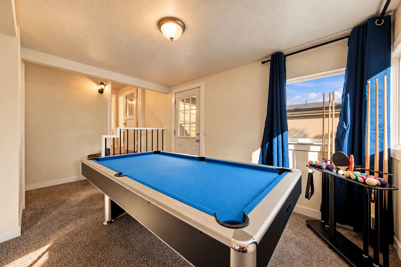 A pool table in a room with a view of the outdoors, a door, and a rack of pool balls.