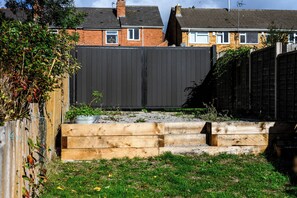 A residential backyard with a raised wooden planter bed, a black fence, and a grassy area. - Renovated, 2 Baths, 2 Lounges, Parking & Garden (Oldbury)